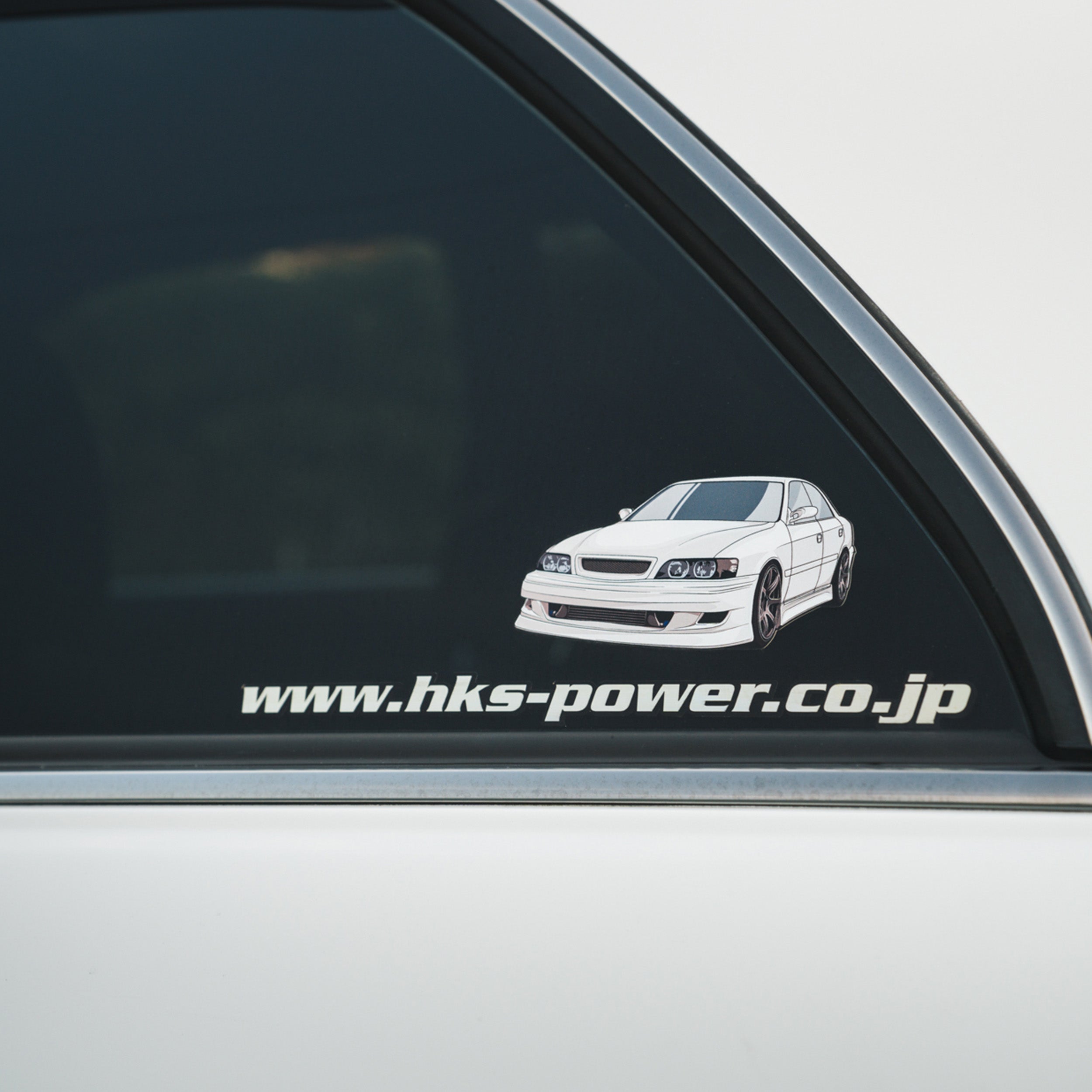 The Toyota Chaser - Slap Sticker by Blossom Automotive features an illustrated white sports sedan with visible door and window frame, plus www.hks-power.co.jp in bold white text.