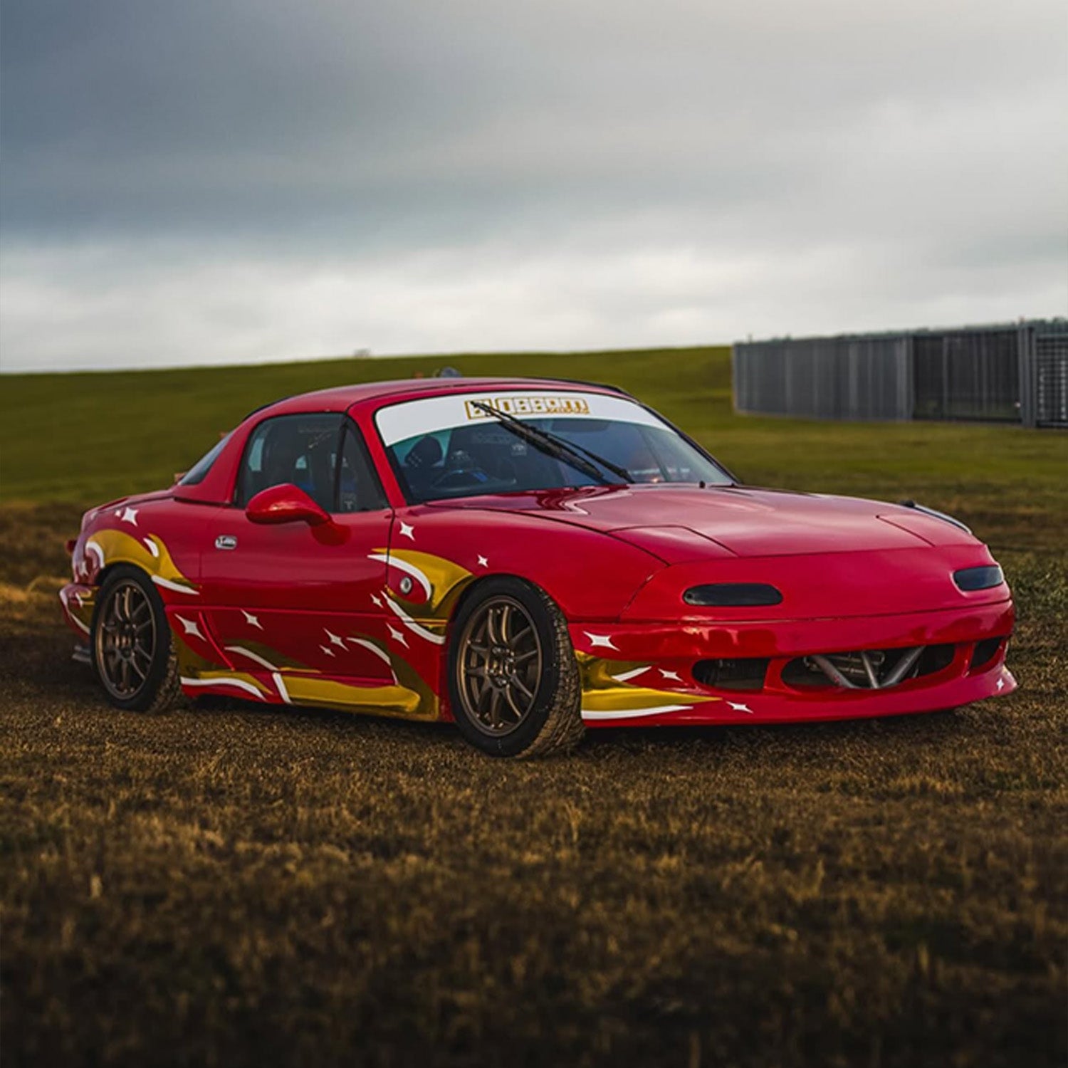 Red sports car with Blossom Automotive Zoku flame design on a grassy field