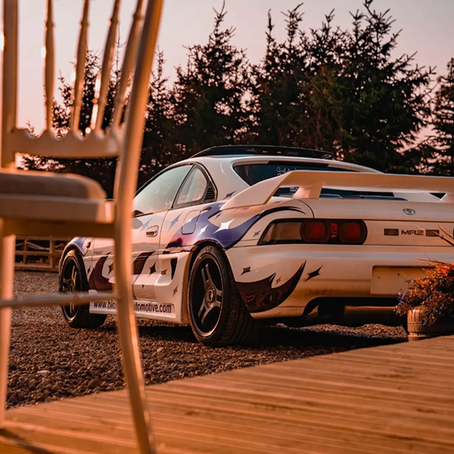 White sports car with purple design parked outdoors with trees in the background