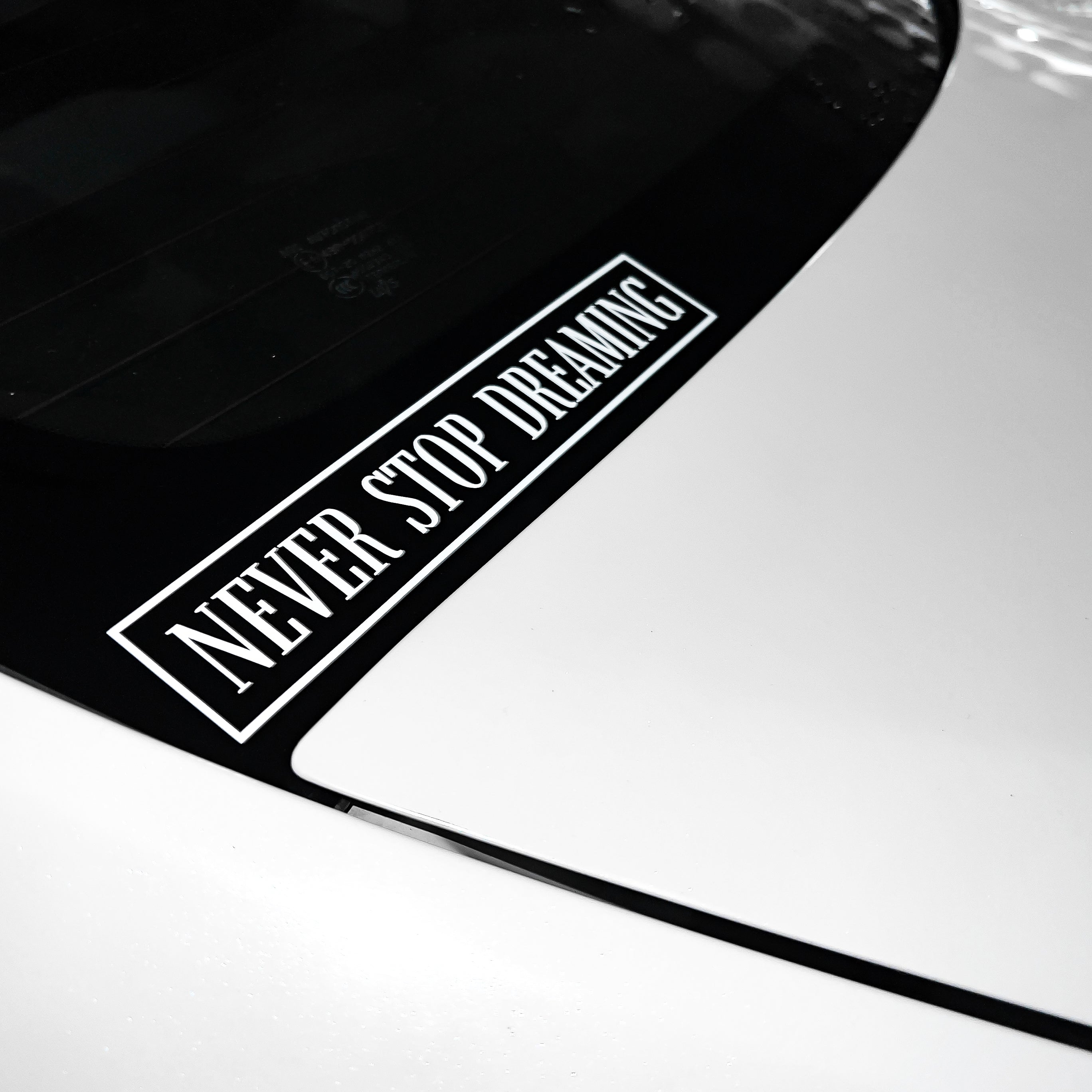 A white car with a Blossom Automotive Never Stop Dreaming - Die Cut Sticker in black and white on its rear window.