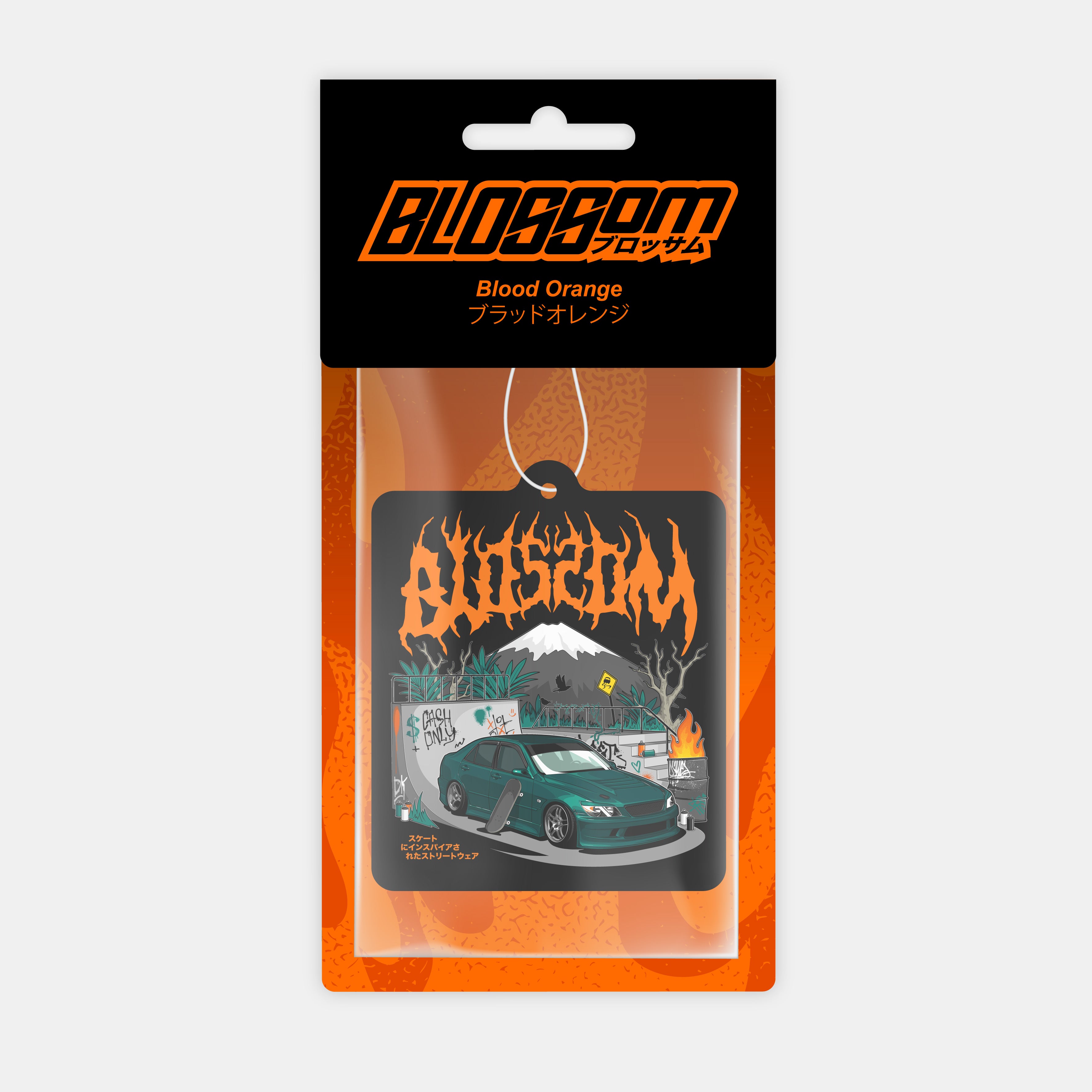 A packaged 'The Skate Collection' Blood Orange air freshener by Blossom Automotive features Japanese text, a teal car drifting before graffiti and flames, with "Blossom" in bold orange jagged letters above.