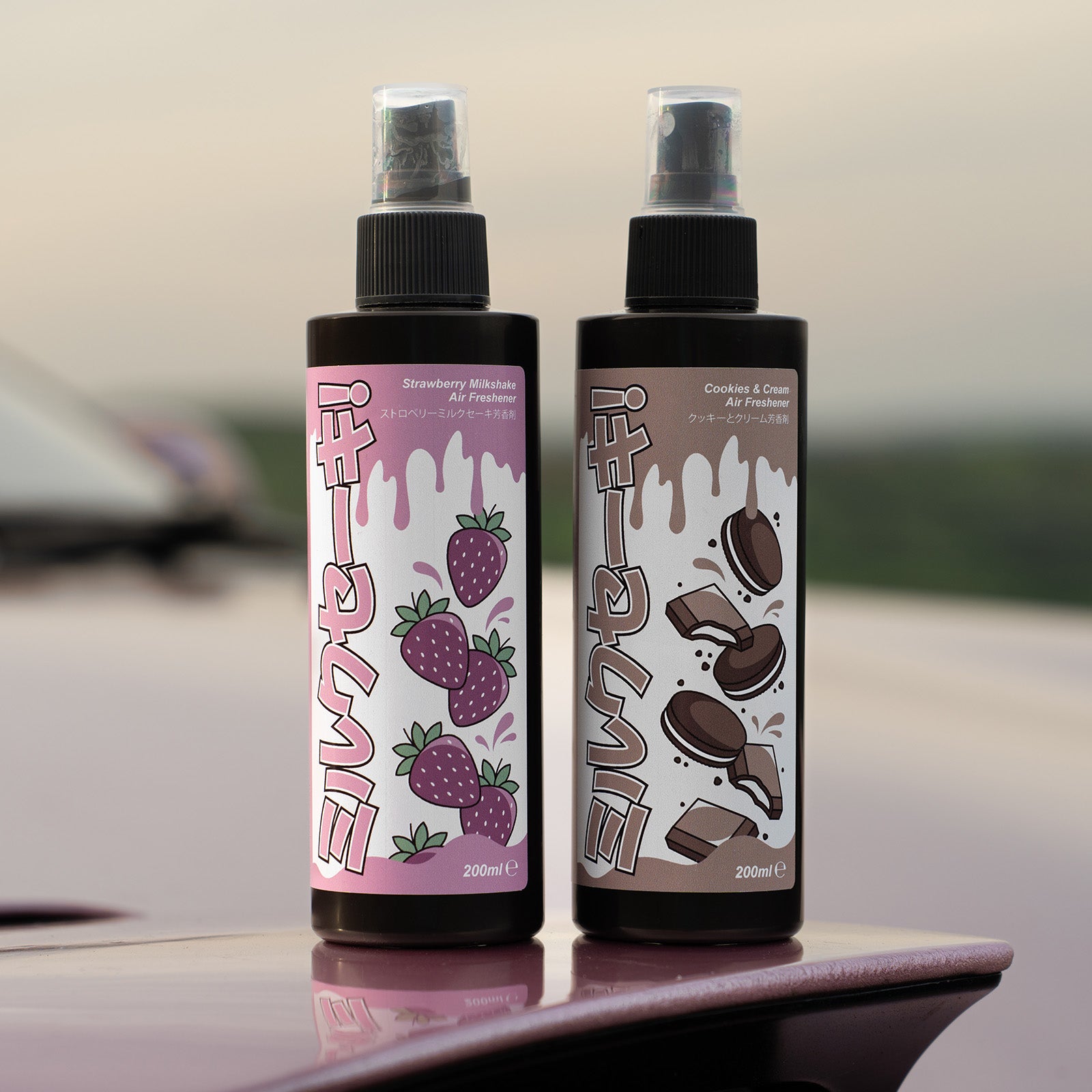 Two 200ml bottles from Blossom Automotive's 'The Milkshake Collection' Car Spray Air Freshener—Strawberry Milkshake and Cookies & Cream—feature playful, cartoon-style labels with black caps, strawberry, and cookie illustrations.