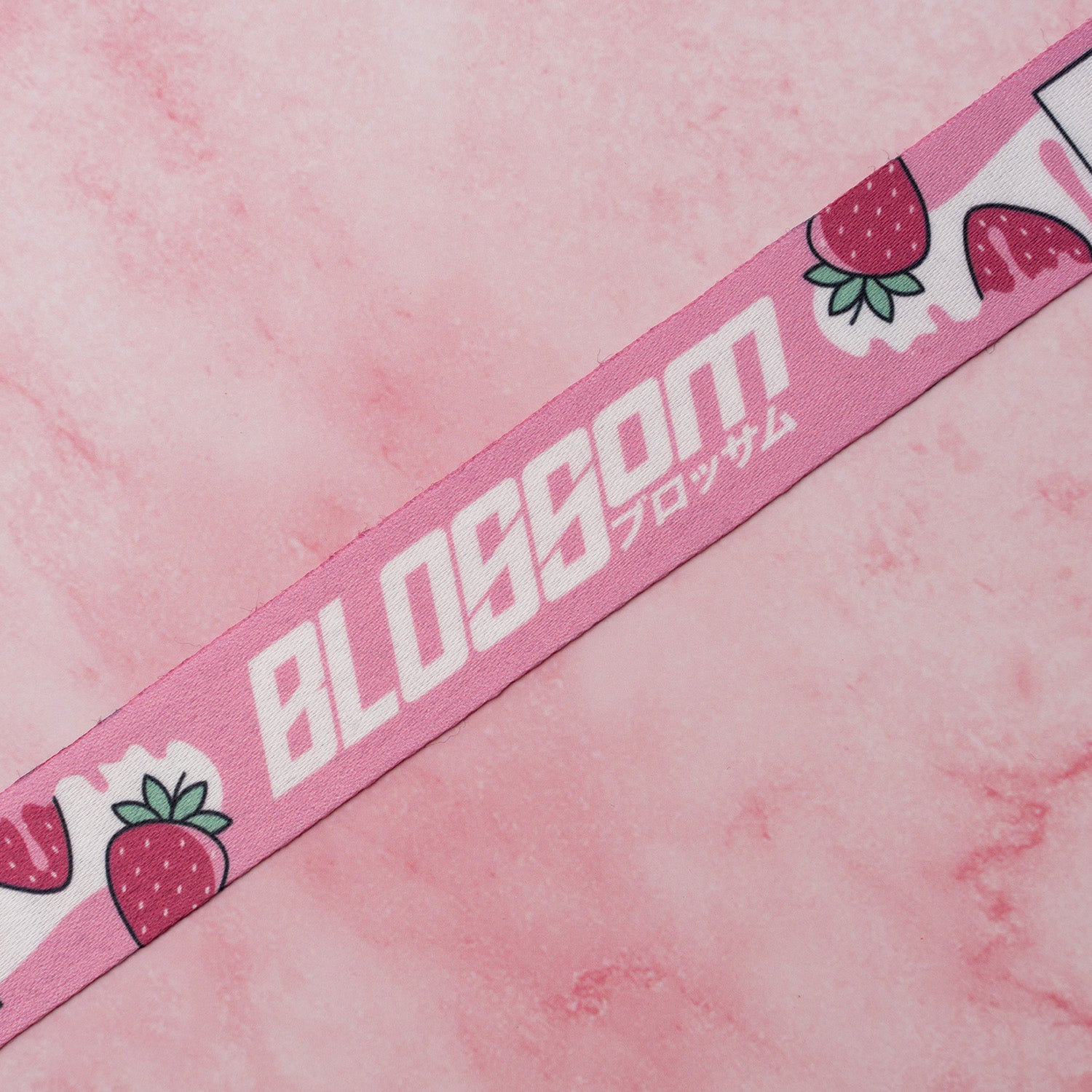A pink strap from Blossom Automotive's 'The Milkshake Collection,’ featuring strawberries, white BLOSSOM text with Japanese characters, on a pink marble background.