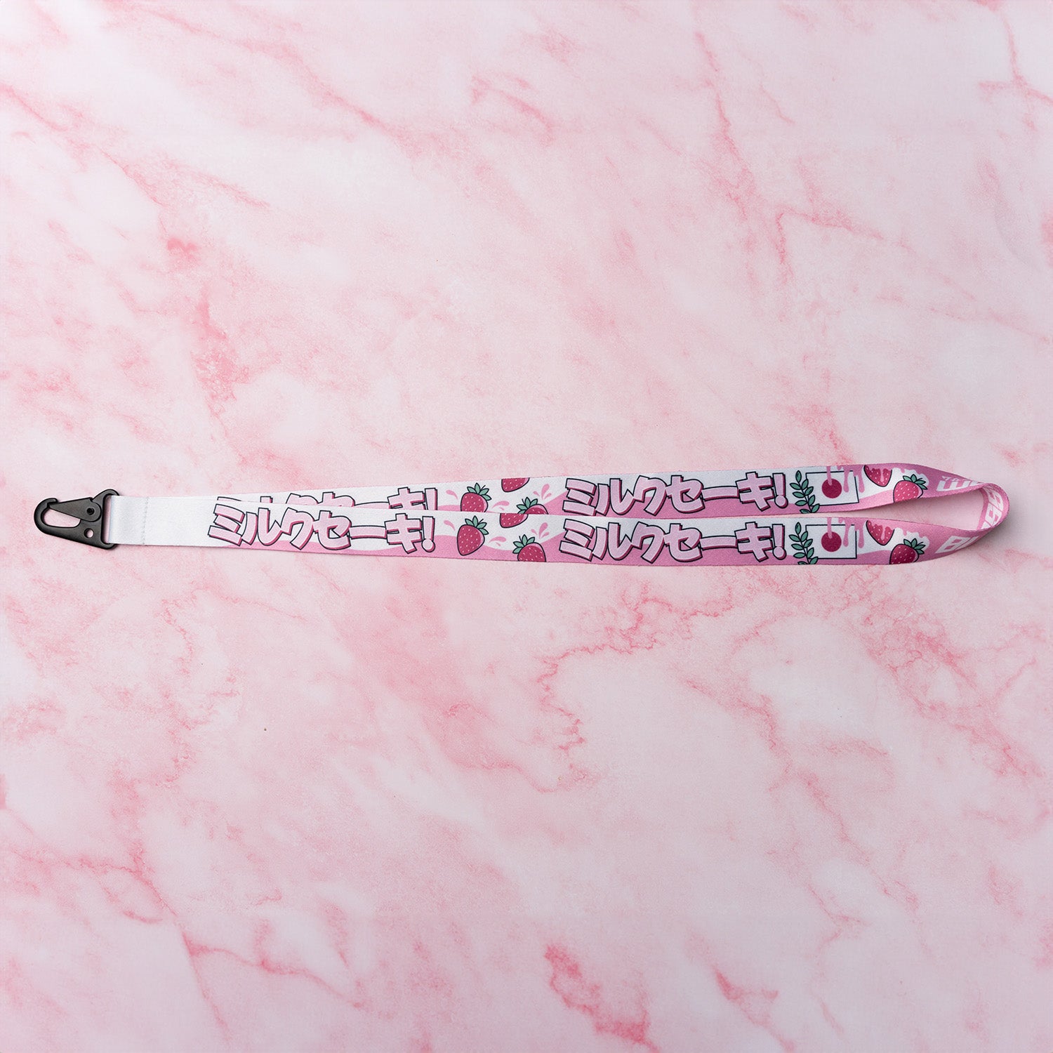 Blossom Automotive's 'The Milkshake Collection’ Lanyard features pink strawberries and Japanese katakana on white, displayed flat on pink marble with a black plastic clip at one end.