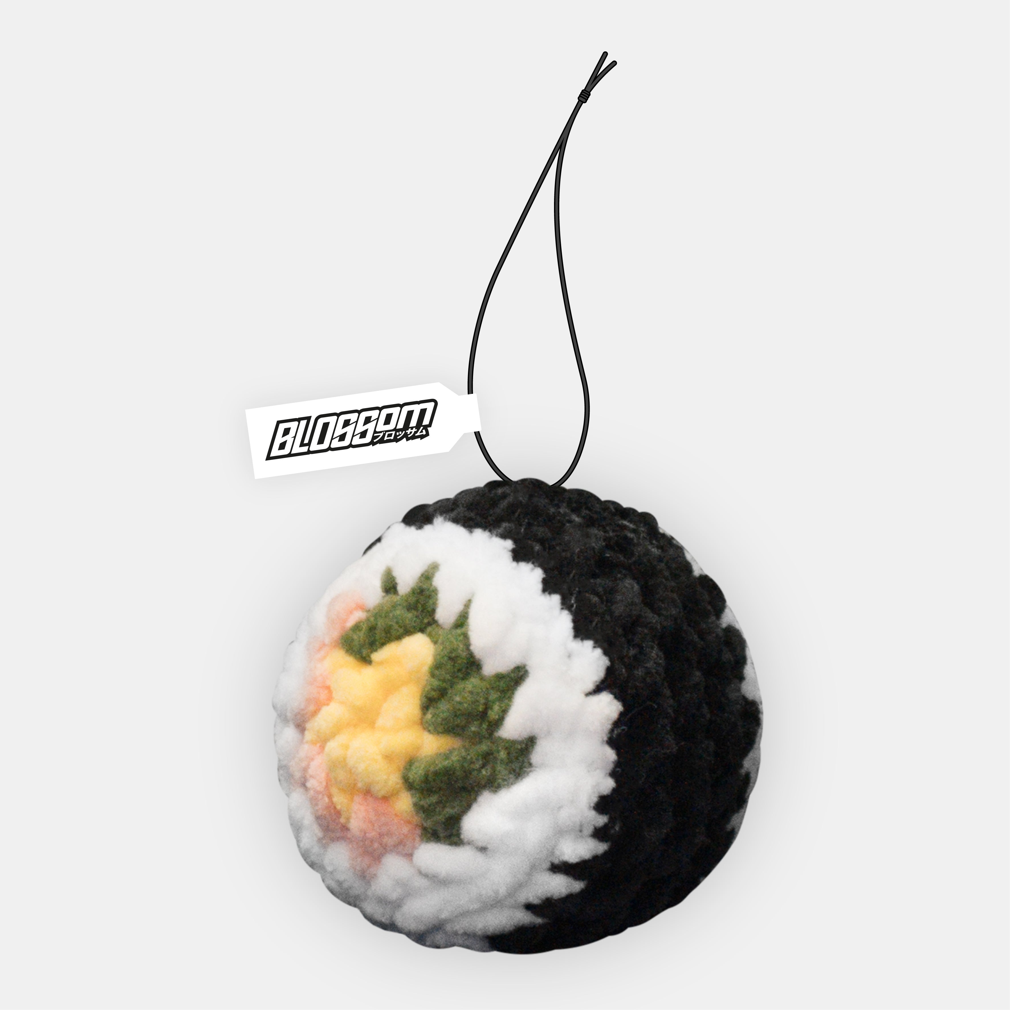The Squishy Sushi - Car Mirror Hanger by Blossom Automotive is a round plush toy resembling a sushi roll, featuring black and white layers with colorful filling, attached to a black string and a white tag labeled BLOSSOM.