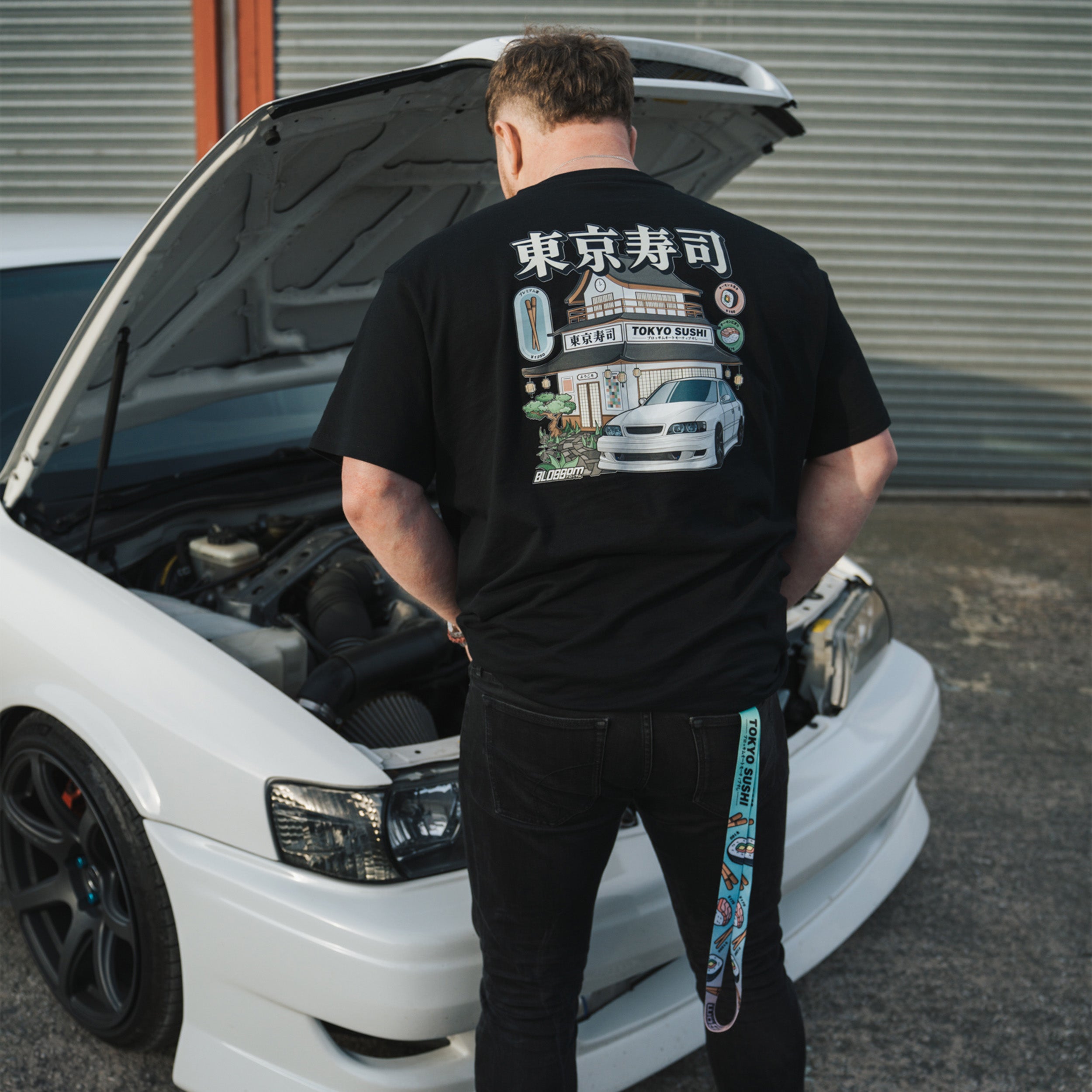 Person stood in front of white Toyota chaser wearing black tee with Tokyo Sushi graphic design on it