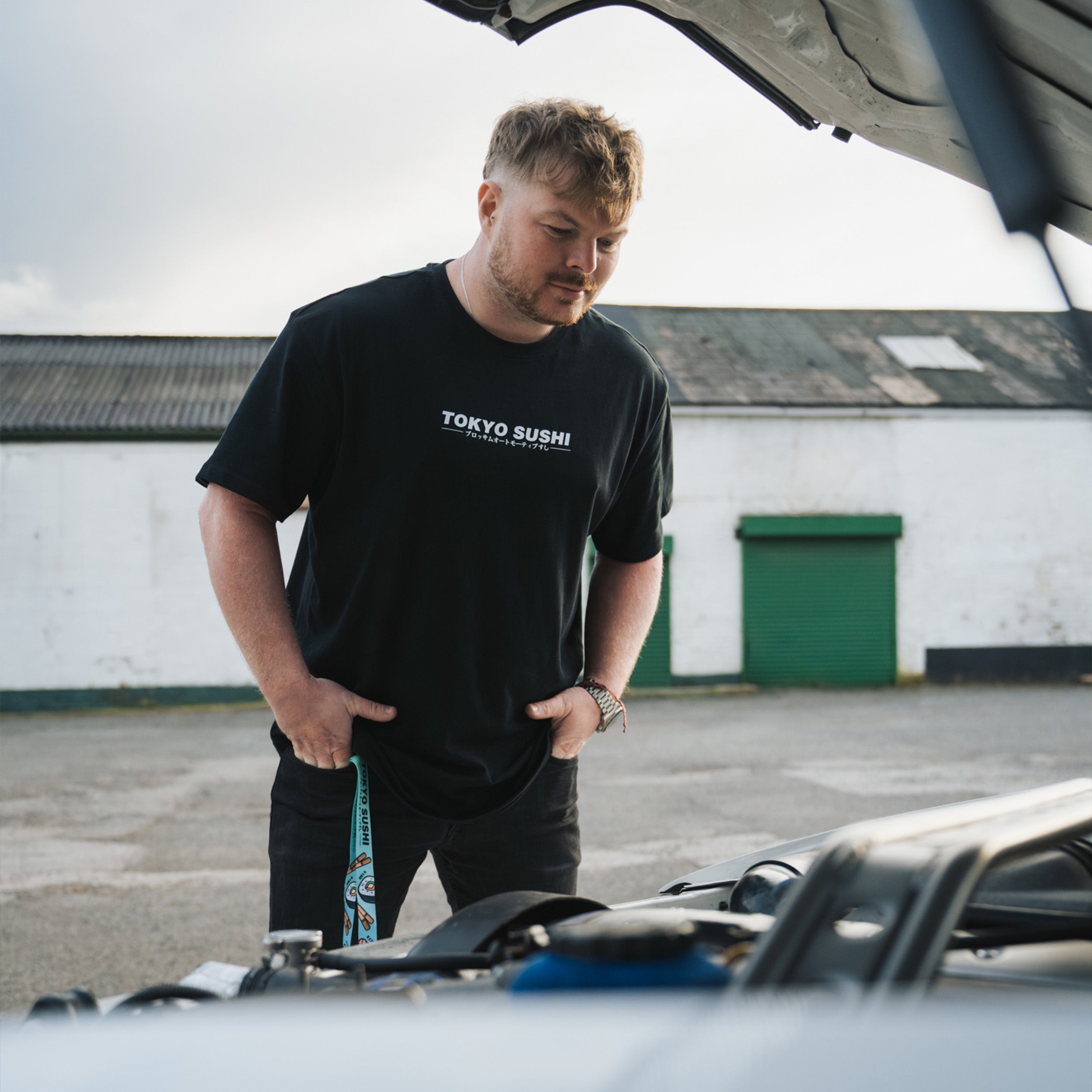 person wearing black Tokyo Sushi tee standing infront of white Toyota chaser