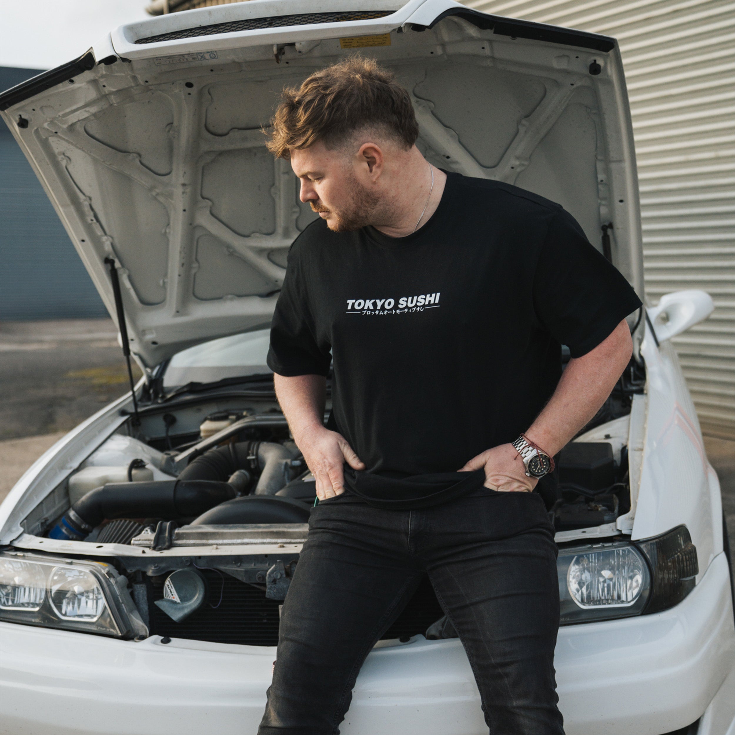 Person sitting on white Toyota chaser while wearing a black Tokyo Sushi Collection tee