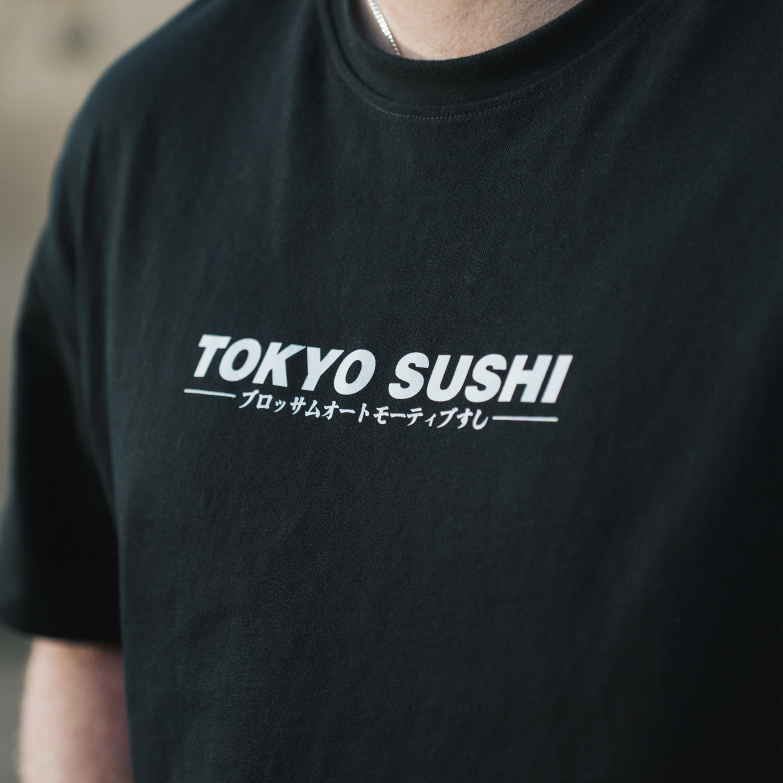 A person wearing a black Tokyo sushi collection t-shirt with a graphic design on the front