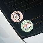 Two Blossom Automotive "Maki Sushi - Slap Stickers" with salmon sushi art and Japanese text are on a car window: one features a sushi roll labeled ¥160, the other shows salmon nigiri marked ¥175.