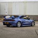 Blue sports car with a sakura floral design parked in front of a building.