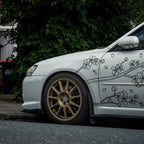 White car with gold rims and floral decals parked on a street.