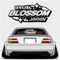A stylized white car with wide tires features the Blossom Japan - XL Rear Window Die-Cut Sticker by Blossom Automotive, and the Blossom Japan logo with Japanese text and sparkles appears above.