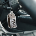 A Blossom Automotive 'The Milkshake Collection' Cookies & Cream air freshener hangs from a car’s steering column, with a brown and white cartoon milk carton design, Japanese text, and coffee bean illustrations in the background.