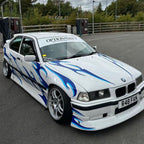 White BMW car with blue flames on a track, featuring the Blossom Enra livery.
