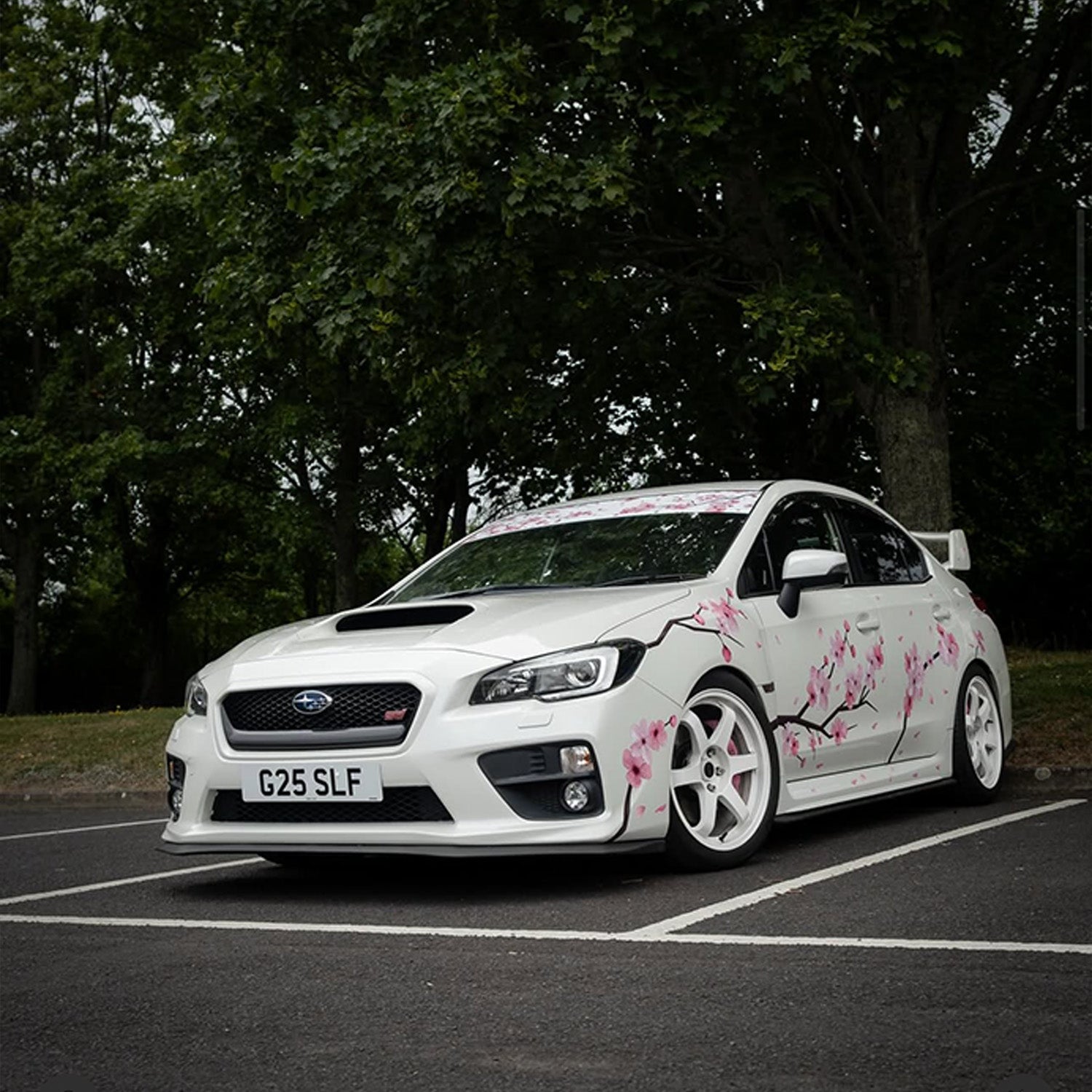 White car with floral Blossom Automotive livery parked in a parking lot with trees in the background