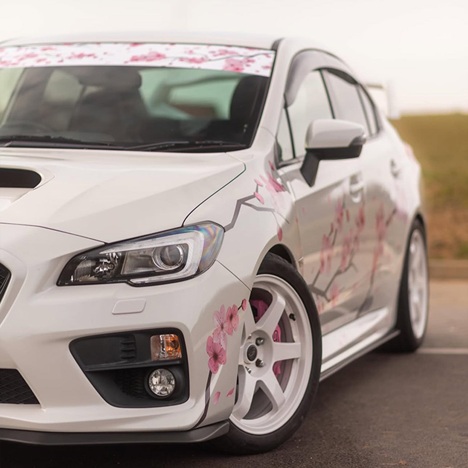 White car with pink floral Blossom Automotive decals on a road