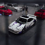 White sports car with purple Zoku decals in a garage with other cars.