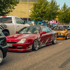 Red car with flame design parked on a street with other vehicles and trees in the background.
