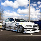 White BMW car with Zoku tribal livery on a parking lot with a blue sky.