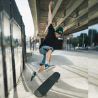 A skateboarder wearing Blossom Automotive’s 'The Skate Collection’ Beanie in Bottle Green performs a mid-air trick at an outdoor skate park beneath a highway overpass on a sunny day.