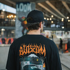 A person wearing the Blossom Automotive 'The Skate Collection’ Cap - Black stands in an urban skate park, facing away from the camera amid graffiti and blurred skaters.