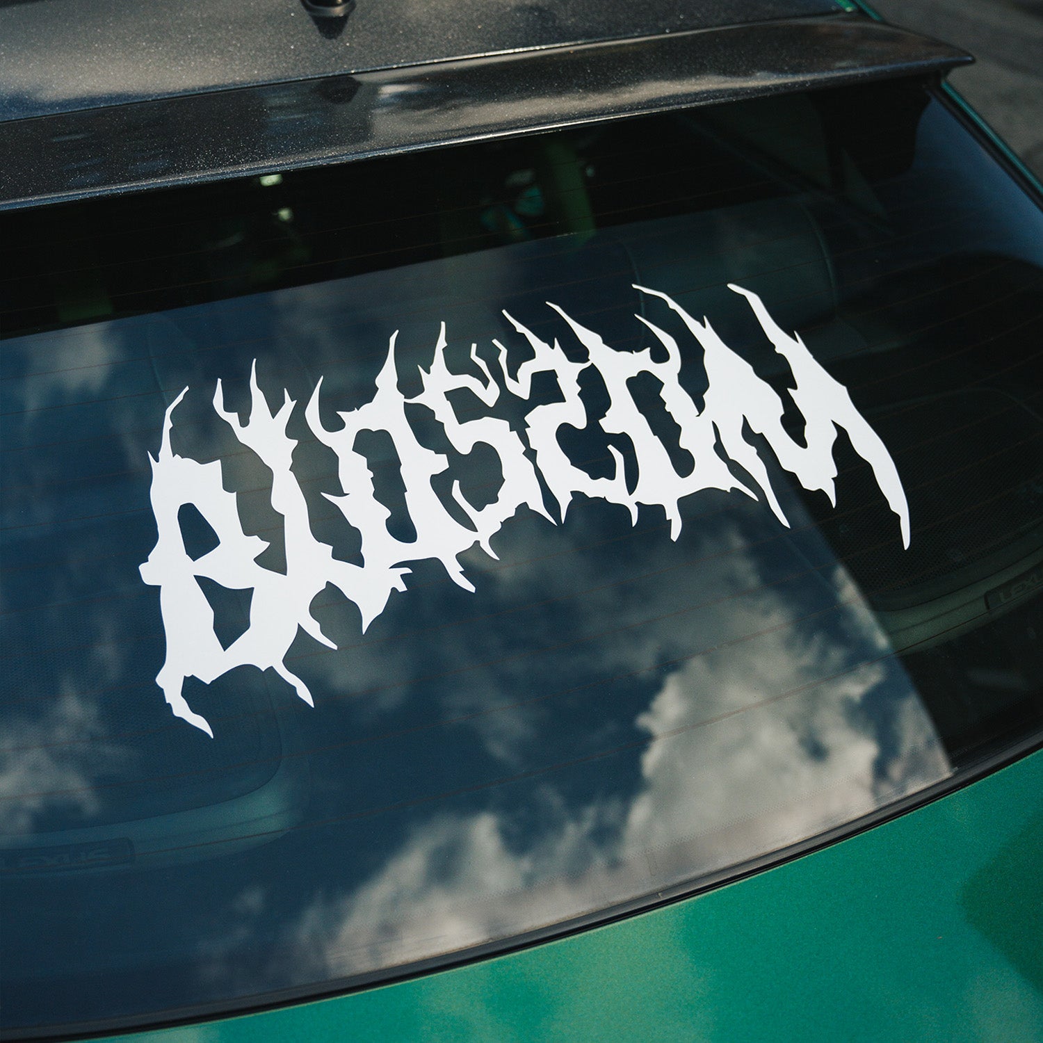 A Blossom Skate Logo - XL Rear Window Die-Cut Sticker from Blossom Automotive is displayed on the rear windshield of a green car, with clouds reflected in the glass.