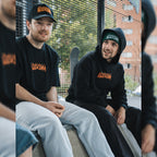 People sat in skatepark while wearing Blossom Skate Collection black tee, hoodie, cap and beanie, featuring Lexus IS200 graphic, oversized fit, inspired by skate and drift culture