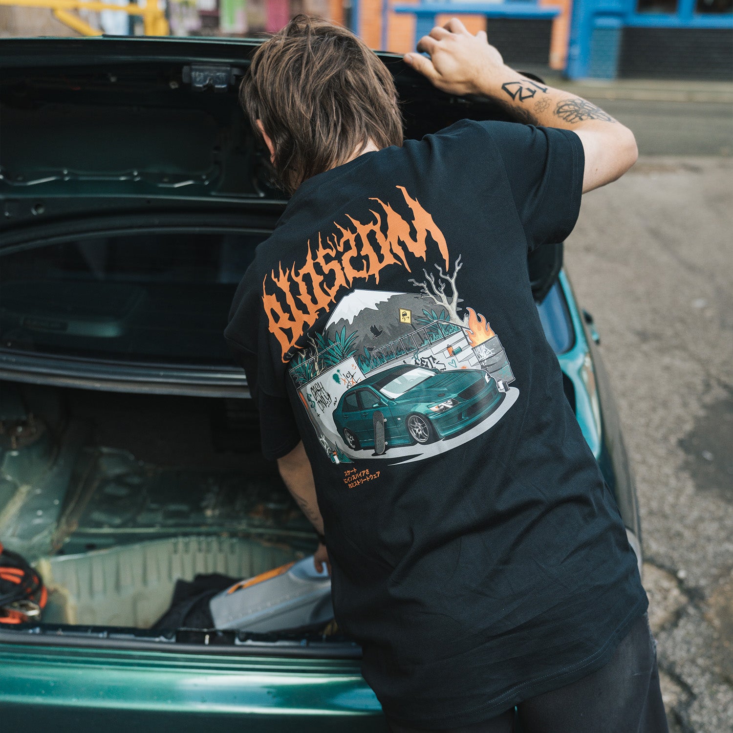 Model standing next to IS200 while wearing Blossom Skate Collection black tee, featuring Lexus IS200 graphic, oversized fit, inspired by skate and drift culture