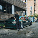 Model leaning on green IS200, wearing Blossom Skate Collection black tee, featuring Lexus IS200 graphic, oversized fit, inspired by skate and drift culture