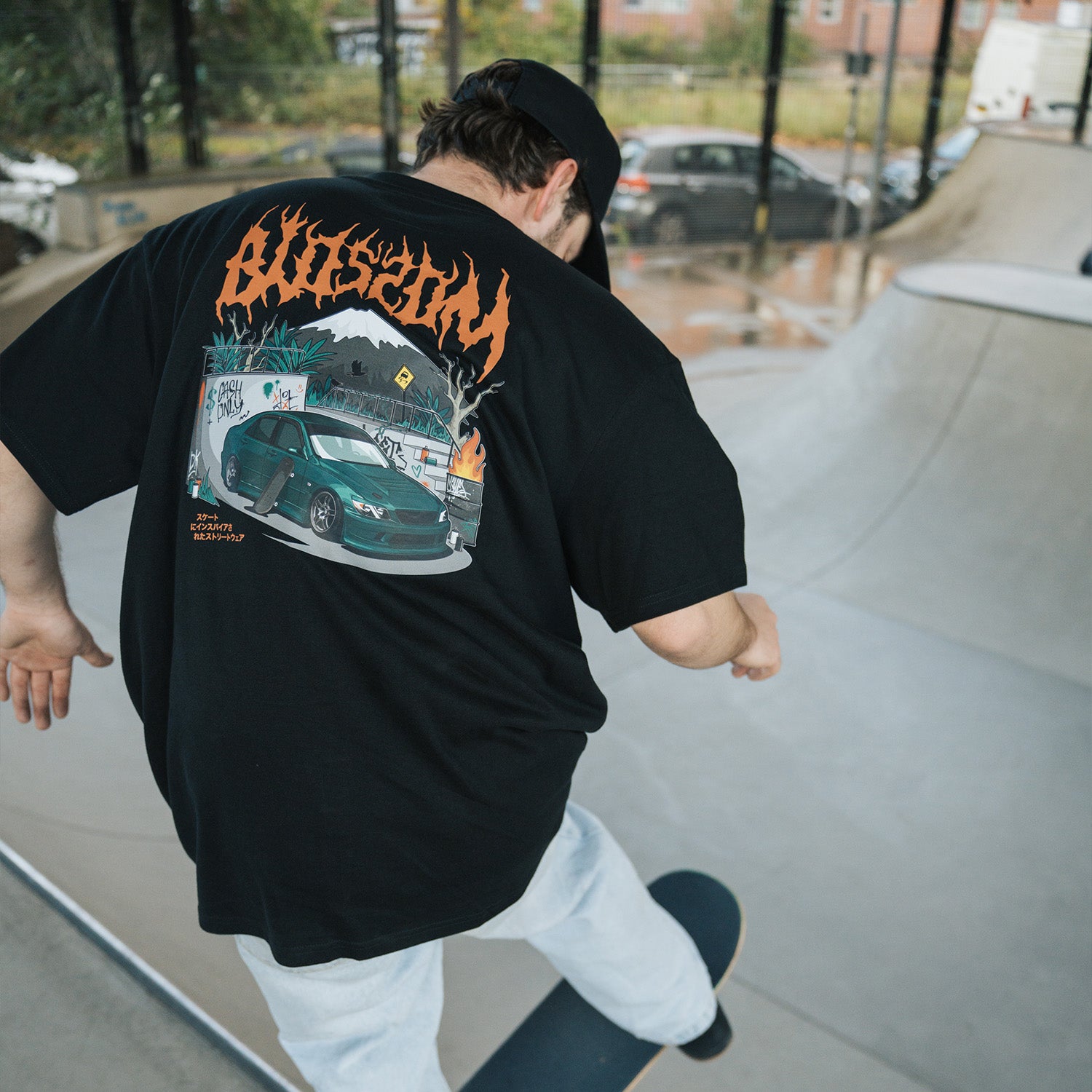 Model skateboarding while wearing Blossom Skate Collection black tee, featuring Lexus IS200 graphic, oversized fit, inspired by skate and drift culture