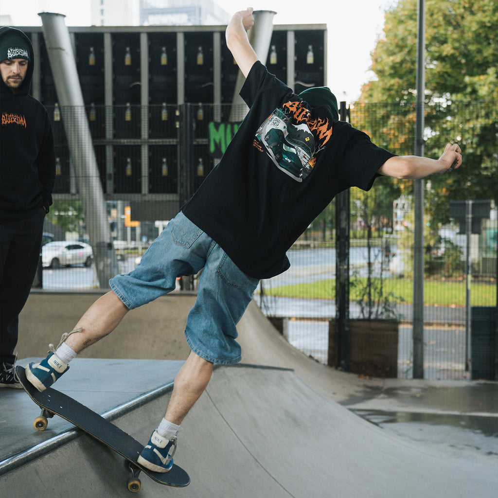 Model skateboarding while wearing Blossom Skate Collection black tee, featuring Lexus IS200 graphic, oversized fit, inspired by skate and drift culture