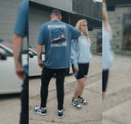 2 people standing by a car wearing the bubblegum collection blue t-shirt and hoodie with pink car on it