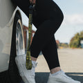 A person in black leggings and white sneakers leans against a light-colored car, holding Blossom Automotive's ‘The Mx5 Collection’ Lanyard. The outdoor scene features a blurred street and buildings in the background.