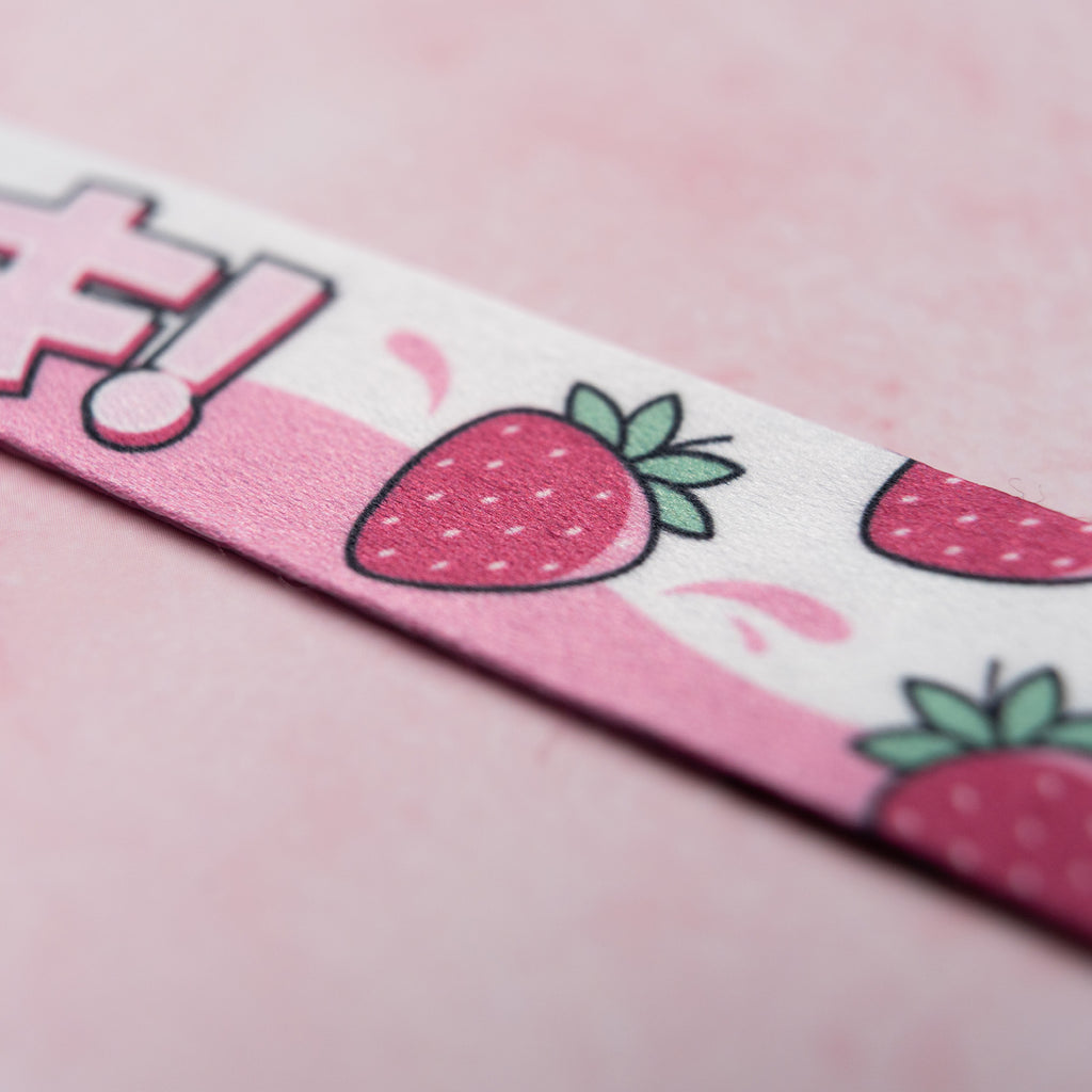 The 'Milkshake Collection' Lanyard by Blossom Automotive features a close-up of pink material adorned with cartoon strawberries and leaves, set against a light pink background.
