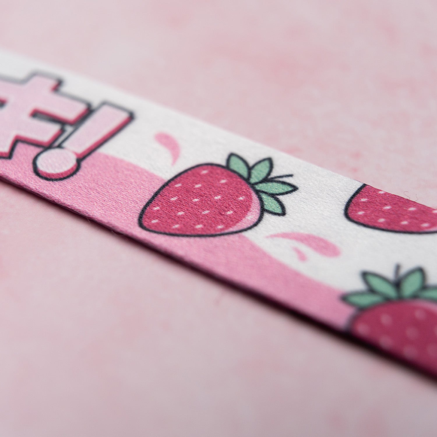 The 'Milkshake Collection' Lanyard by Blossom Automotive features a close-up of pink material adorned with cartoon strawberries and leaves, set against a light pink background.