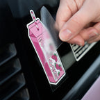 A hand peels a transparent film off a Blossom Automotive Strawberry Milkshake - Slap Sticker, shaped like a pink carton with a straw, shown on a black surface.