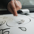 A hand peels a Blossom Automotive Mx5 - Slap Sticker from the fuel cap of a white, floral-patterned car, revealing a barcode.