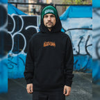 a front shot of a person wearing the black skate collection green beanie and hoodie featuring a skatepark and a green Lexus is200
