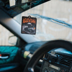 The Blossom Automotive 'The Skate Collection' Air Freshener - Blood Orange, featuring a car graphic and bold "Awesome" text, hangs from a rearview mirror inside a car accented with teal and black.