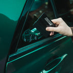 A hand uses the Blossom Automotive IS200 - Slap Sticker squeegee tool to apply a green car sticker onto the rear side window of a green vehicle.