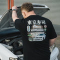 A person wearing a black Tokyo sushi collection t-shirt with a graphic design on the back, featuring a Toyota chaser, standing next to a car.