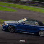 A blue convertible races around a track, showcasing Blossom URL - XL Die-Cut Sticker (x1) by Blossom Automotive on the window and hood. JW Visuals logo is visible at the bottom, with motion blur in the background.