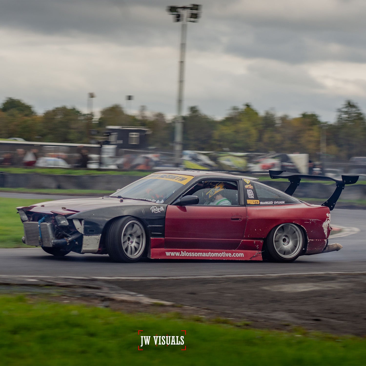 The Blossom Automotive "Blossom URL - XL Die-Cut Sticker (x1)" features a red and black drift car with a large rear wing sliding sideways on a track, tires smoking, missing front bumper, against an overcast backdrop with trees.