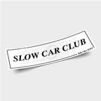 The Blossom Automotive Slow Car Club - Slap Sticker features bold black "SLOW CAR CLUB" lettering, a faint SLOW outline, Japanese text and a website in the corners, all on a white rectangular background.